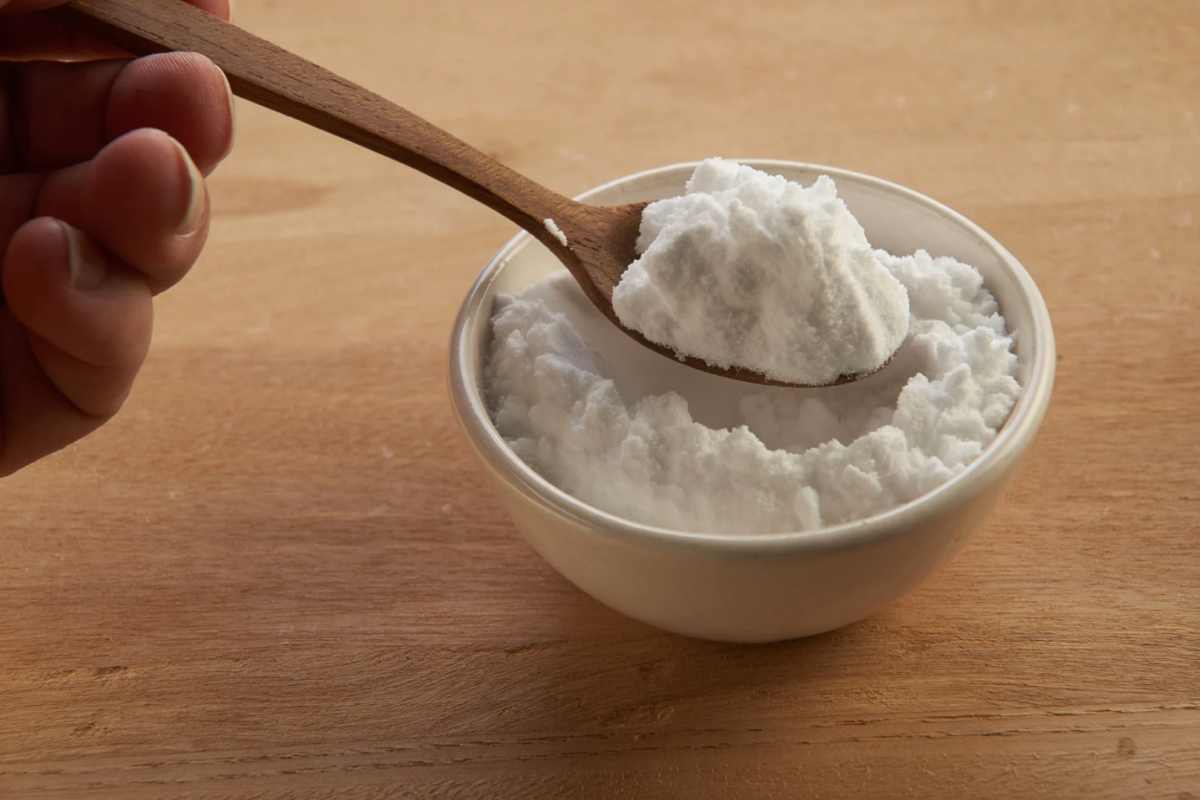Persona che mette un cucchiaio di legno in una ciotola con bicarbonato